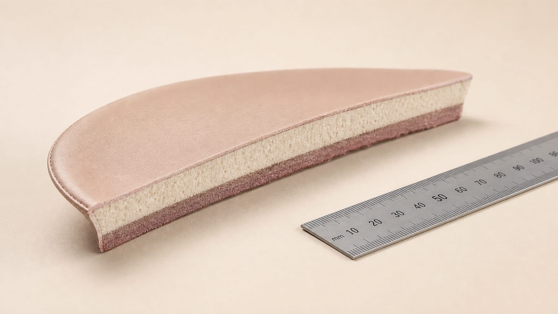 An insole cut in half lengthways and stood on its cut edge, layers visible against a rule.